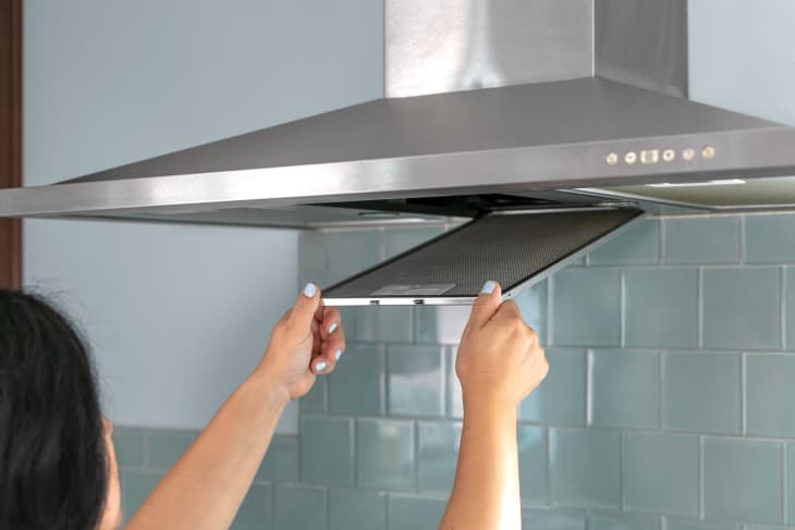 Person removing a grease filter from a stainless steel kitchen range hood