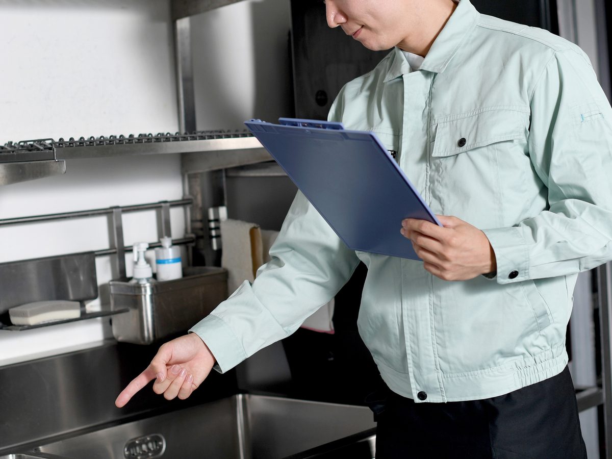Technician with a clipboard assessing equipment in a commercial kitchen