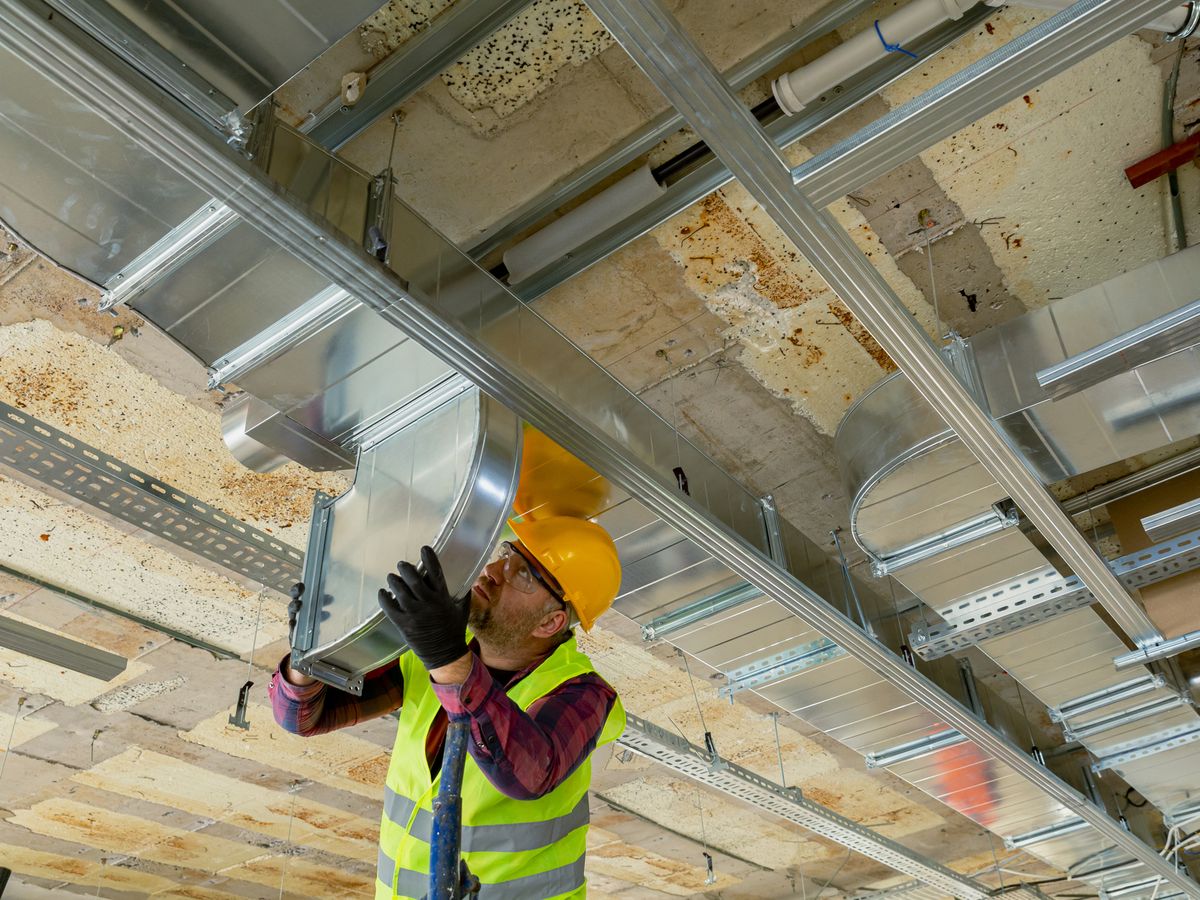Tradesperson in hard hat and hi-vis installing exhaust ductwork overhead