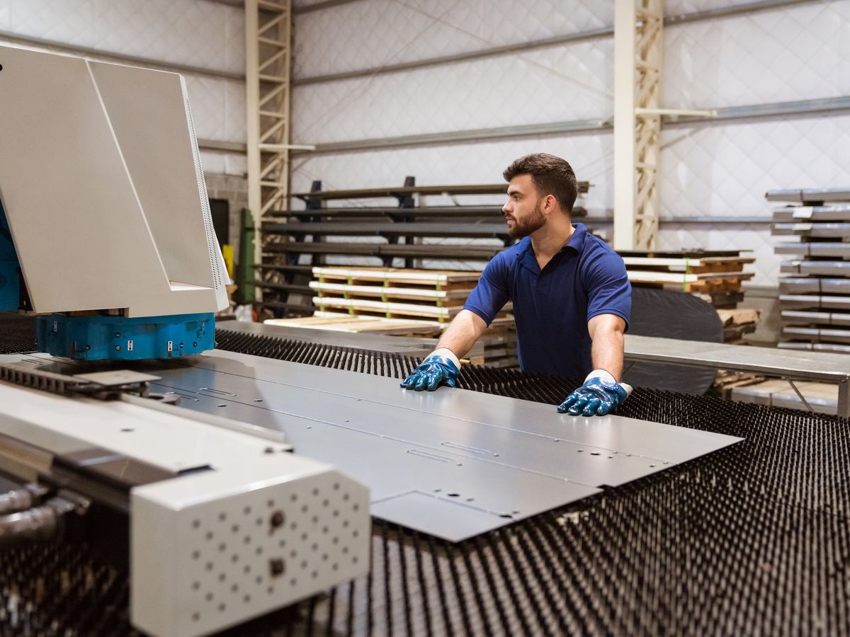 Fabricator handling stainless steel sheet on a workshop machine