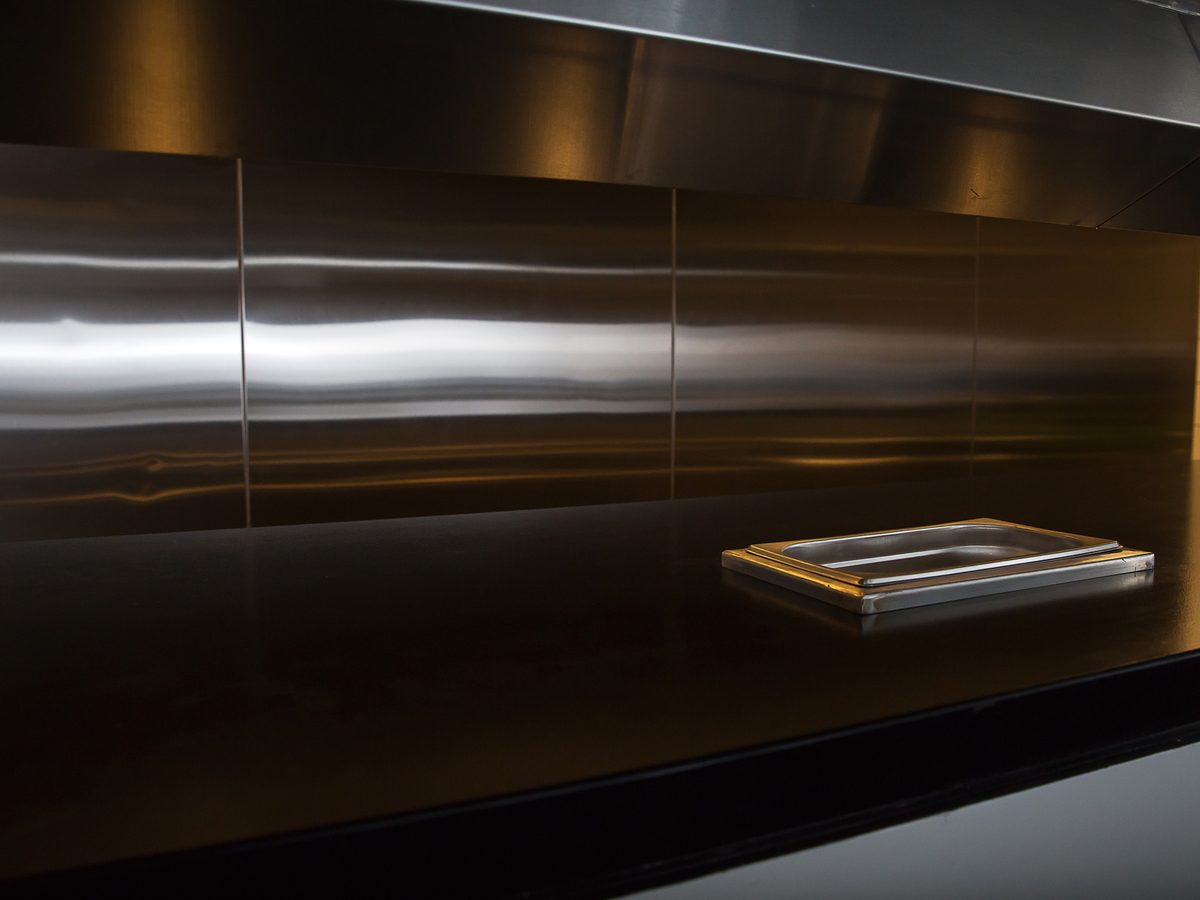Seamless brushed stainless steel splashback panels above a commercial kitchen bench