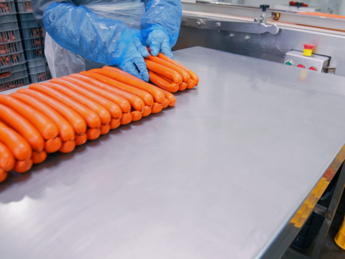 Worker in gloves handling sausages on a stainless steel production workbench