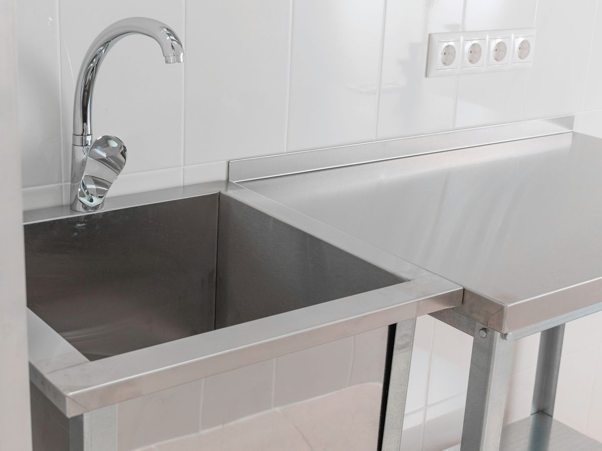 Close-up of a stainless steel sink bench with a formed backsplash upstand